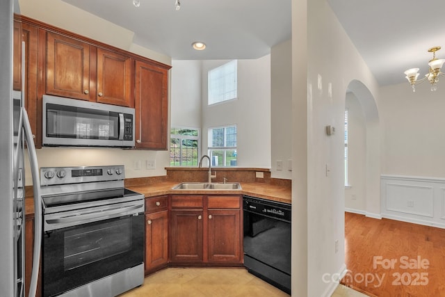 5963 Pale Moss Ln, Charlotte, NC 28269 - kitchen with appliances with stainless steel finishes, a sink, a chandelier, arched walkways, and brown cabinetry