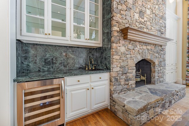 517 Kingsdown Ct, Waxhaw, NC 28173 - indoor wet bar featuring wine cooler, light wood finished floors, decorative backsplash, and a stone fireplace