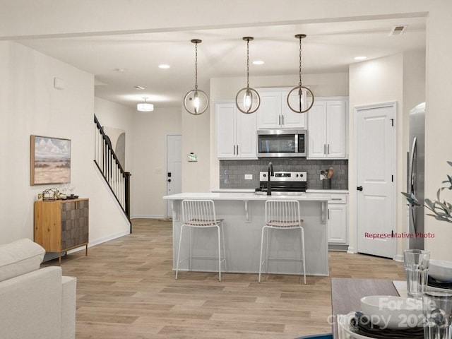 12016 Basking Dr, Charlotte, NC 28214 - kitchen featuring stainless steel appliances, decorative backsplash, light countertops, light wood-type flooring, and white cabinets