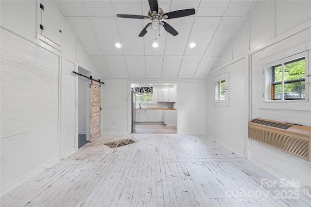220 W College St, Black Mountain, NC 28711 - unfurnished living room with a barn door, light wood-type flooring, vaulted ceiling, ceiling fan, and a wall unit AC