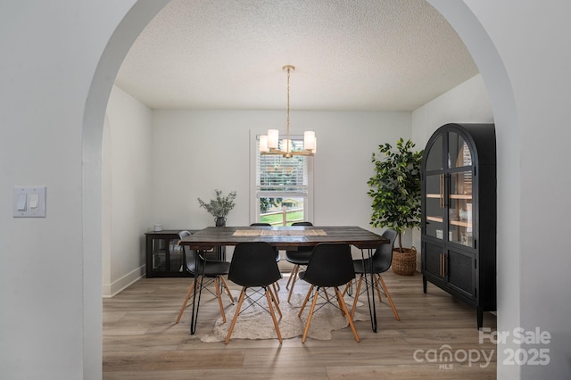1256 Canseco Ln, Hickory, NC 28602 - dining room with light wood-type flooring, a chandelier, a textured ceiling, and arched walkways