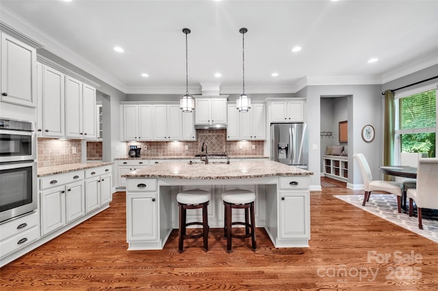 1600 Buckland Ct, Indian Land, SC 29707 - kitchen with appliances with stainless steel finishes, a breakfast bar, a kitchen island with sink, wood finished floors, and crown molding