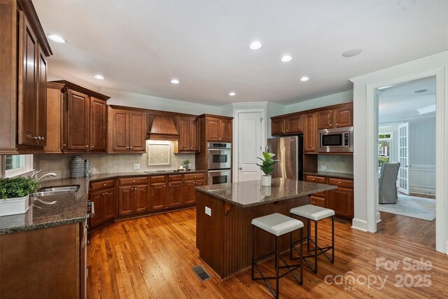 7319 Stonehaven Dr, Waxhaw, NC 28173 - kitchen with stainless steel appliances, a sink, custom exhaust hood, light wood-type flooring, and a kitchen breakfast bar
