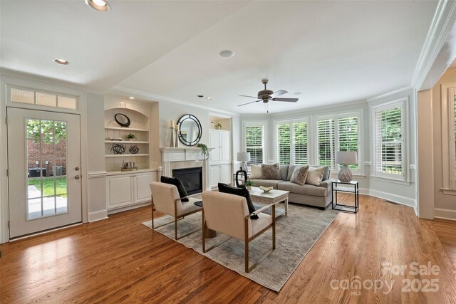 7319 Stonehaven Dr, Waxhaw, NC 28173 - living area featuring ornamental molding, a glass covered fireplace, light wood finished floors, built in features, and ceiling fan