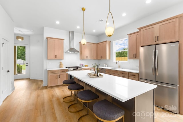 2413 Pruitt St, Charlotte, NC 28208 - kitchen with appliances with stainless steel finishes, wall chimney range hood, a breakfast bar area, light brown cabinetry, and light wood-style flooring
