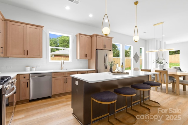 2413 Pruitt St, Charlotte, NC 28208 - kitchen featuring appliances with stainless steel finishes, light wood-style flooring, decorative backsplash, a breakfast bar, and light countertops
