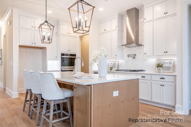 1059 Sage Pine Cir Unit 56, Clover, SC 29710 - kitchen with wall chimney exhaust hood, a chandelier, appliances with stainless steel finishes, white cabinetry, and a kitchen island with sink