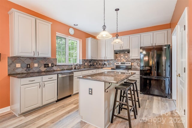 8219 Beardsley Dr, Charlotte, NC 28269 - kitchen featuring appliances with stainless steel finishes, under cabinet range hood, light wood finished floors, a kitchen island, and a sink