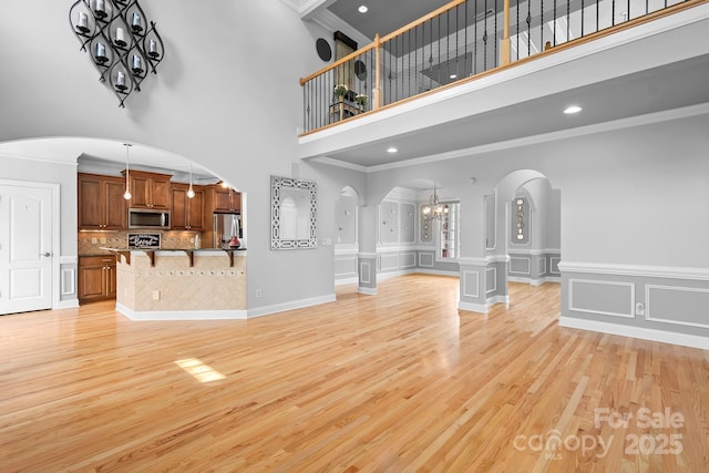 9112 Butterfly Ct, Gastonia, NC 28056 - unfurnished living room with arched walkways, a chandelier, a high ceiling, ornamental molding, and light wood finished floors