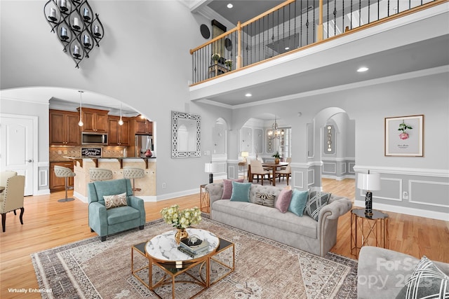 9112 Butterfly Ct, Gastonia, NC 28056 - living room featuring arched walkways, a towering ceiling, ornamental molding, light wood-style floors, and a chandelier