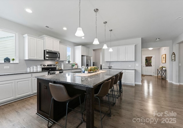 204 Fesperman Cir, Troutman, NC 28166 - kitchen featuring appliances with stainless steel finishes, a kitchen island, decorative backsplash, a breakfast bar, and white cabinetry