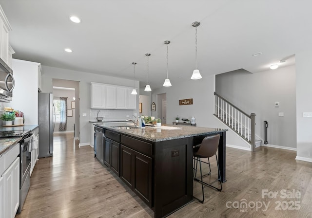 204 Fesperman Cir, Troutman, NC 28166 - kitchen featuring stainless steel appliances, a center island with sink, white cabinets, light stone countertops, and light wood-style floors