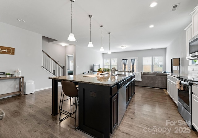 204 Fesperman Cir, Troutman, NC 28166 - kitchen with stainless steel appliances, a breakfast bar area, open floor plan, dark wood-style flooring, and dark stone counters