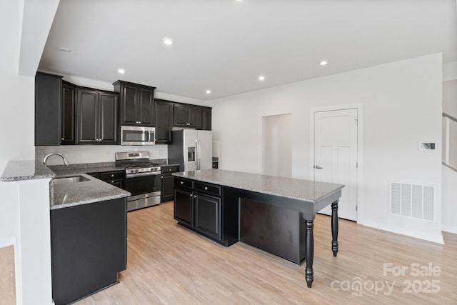 207 Welcombe St, Mooresville, NC 28115 - kitchen with stainless steel appliances, a sink, dark cabinetry, a kitchen island, and light wood-style floors