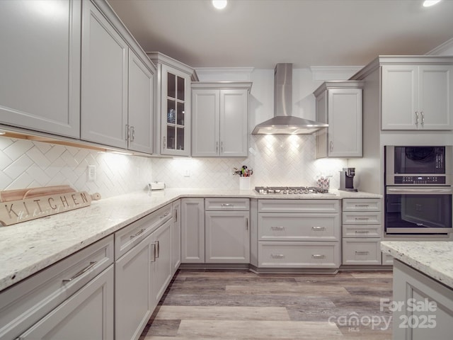 647 R L Stowe Rd, Belmont, NC 28012 - kitchen with wall chimney range hood, appliances with stainless steel finishes, light wood-style floors, tasteful backsplash, and light stone countertops