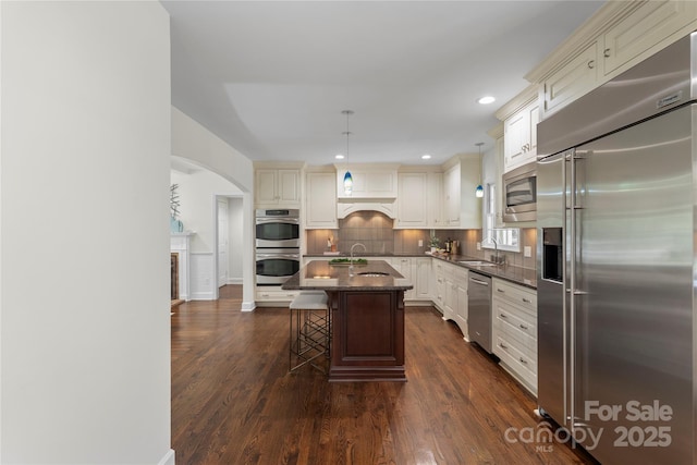 7213 Lancer Dr, Charlotte, NC 28226 - kitchen featuring built in appliances, a sink, arched walkways, a breakfast bar, and dark wood-style flooring