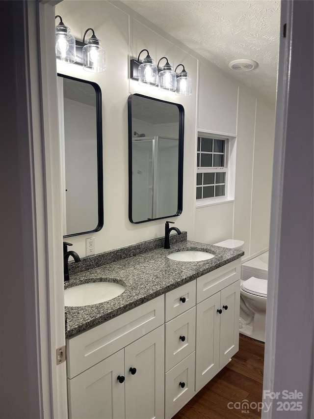 6219 Heavner Rd, Vale, NC 28168 - bathroom featuring a shower, double vanity, a textured ceiling, wood finished floors, and toilet