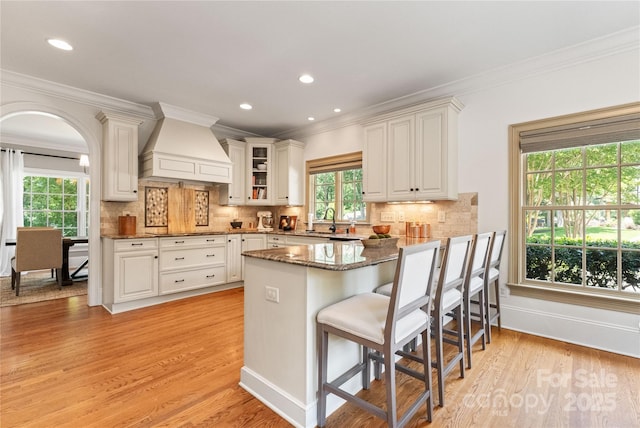 901 Hartford Ave, Charlotte, NC 28209 - kitchen featuring wall chimney exhaust hood, light wood finished floors, a sink, crown molding, and a peninsula