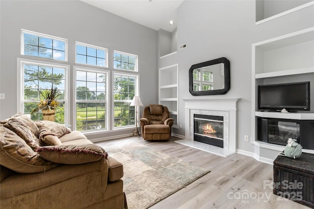 7704 Ninth Fairway Ln, Mint Hill, NC 28227 - living room featuring built in shelves, a fireplace, a towering ceiling, and wood finished floors