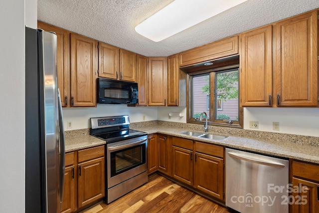204 Woodfield Dr, Asheville, NC 28803 - kitchen featuring appliances with stainless steel finishes, light wood-style floors, brown cabinetry, a textured ceiling, and light stone countertops