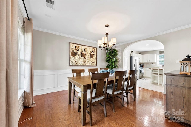 4612 Maple Crest Pl, Harrisburg, NC 28075 - dining room featuring arched walkways, crown molding, light wood-type flooring, a chandelier, and a wainscoted wall