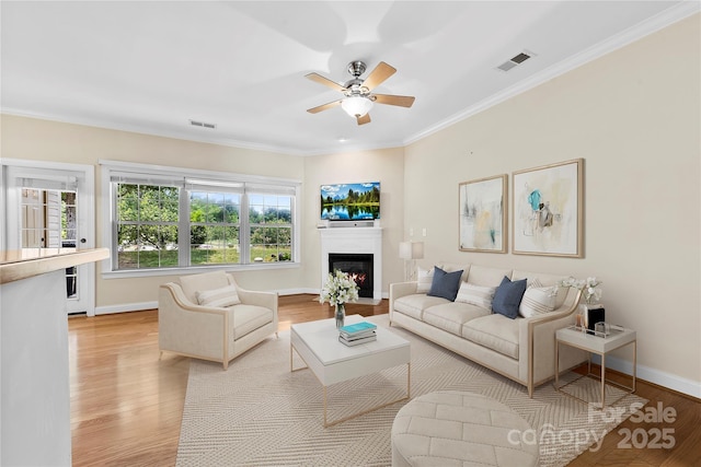 2765 Clover Rd NW, Concord, NC 28027 - living room featuring a ceiling fan, light wood-type flooring, a warm lit fireplace, ornamental molding, and baseboards