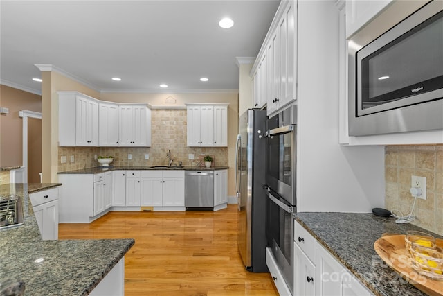 1336 Dobson Dr, Waxhaw, NC 28173 - kitchen with stainless steel appliances, backsplash, white cabinetry, crown molding, and light wood-style flooring