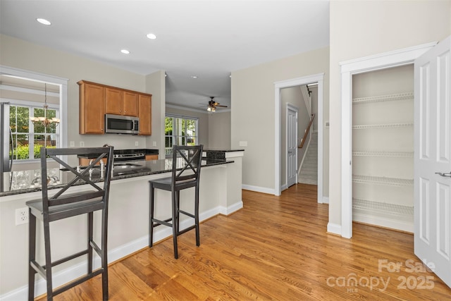 187 Water Oak Dr, Mooresville, NC 28117 - kitchen featuring stainless steel appliances, brown cabinetry, a breakfast bar area, light wood-type flooring, and dark stone counters