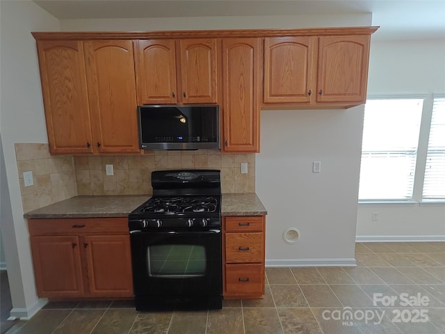 509 Settlers Grove Ln, Salisbury, NC 28146 - kitchen featuring stainless steel microwave, black range with gas stovetop, light stone counters, tasteful backsplash, and brown cabinetry