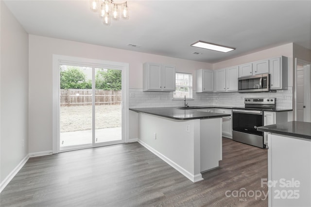 7806 Mcgarry Trl, Charlotte, NC 28214 - kitchen with stainless steel appliances, dark countertops, decorative backsplash, dark wood-type flooring, and a peninsula