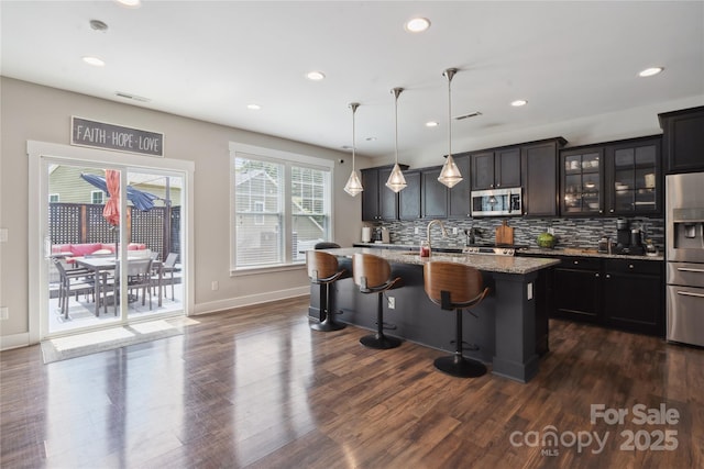 10012 Michael Crossing Dr, Charlotte, NC 28213 - kitchen featuring stainless steel appliances, a breakfast bar, backsplash, a center island with sink, and glass insert cabinets
