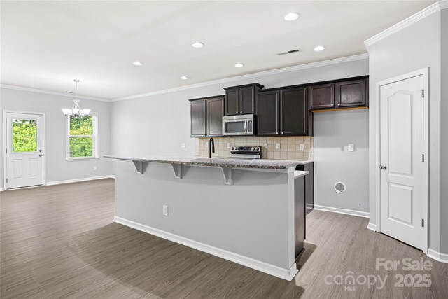 8400 Empress Ct, Charlotte, NC 28227 - kitchen with appliances with stainless steel finishes, a kitchen island with sink, a chandelier, light wood-style flooring, and baseboards