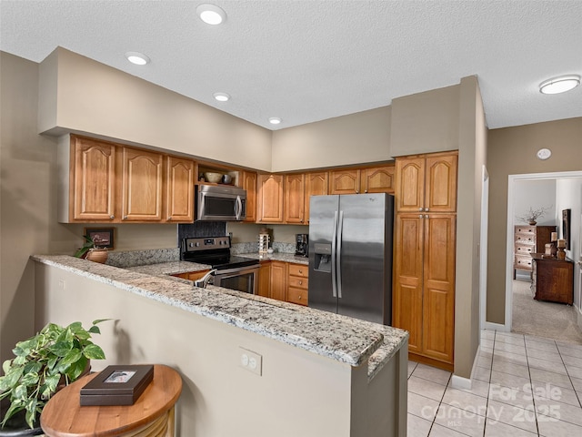 306 Croydon Dr, Hendersonville, NC 28791 - kitchen featuring stainless steel appliances, a peninsula, light tile patterned floors, a textured ceiling, and brown cabinetry