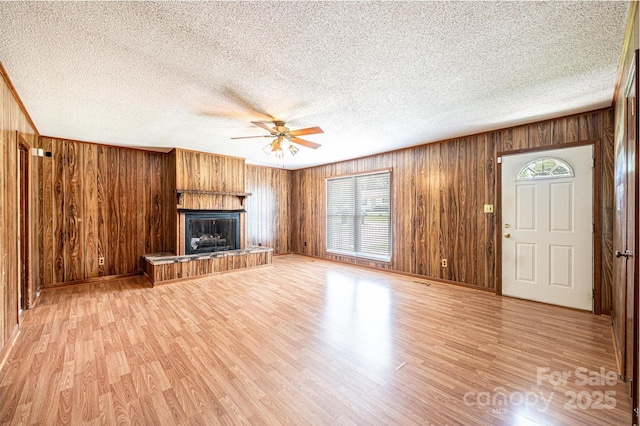 2031 36th St NE, Hickory, NC 28601 - unfurnished living room featuring ceiling fan, wooden walls, a fireplace with raised hearth, light wood-style flooring, and a textured ceiling