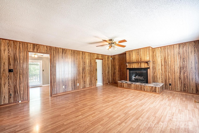 2031 36th St NE, Hickory, NC 28601 - unfurnished living room with a ceiling fan, wood walls, light wood-style floors, a fireplace with raised hearth, and a textured ceiling