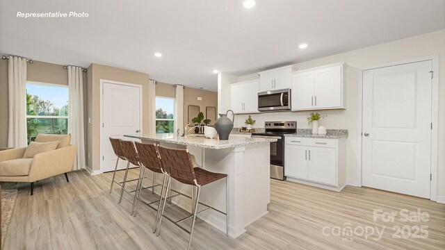 4689 Fanning Rd, Hickory, NC 28602 - kitchen featuring stainless steel appliances, light wood-type flooring, a kitchen breakfast bar, an island with sink, and light stone counters
