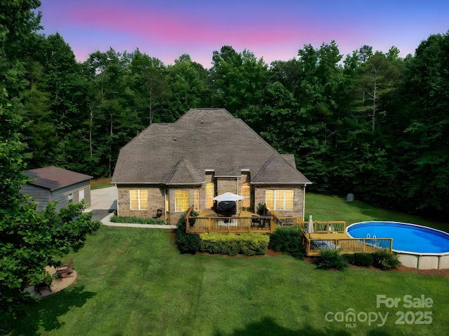 8101 Cane Pointe Ln, Waxhaw, NC 28173 - back of property at dusk with a wooden deck, an outdoor pool, brick siding, a yard, and a wooded view