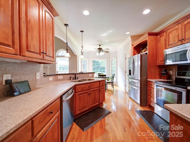 8101 Cane Pointe Ln, Waxhaw, NC 28173 - kitchen featuring stainless steel appliances, a sink, ornamental molding, brown cabinetry, and light wood-type flooring