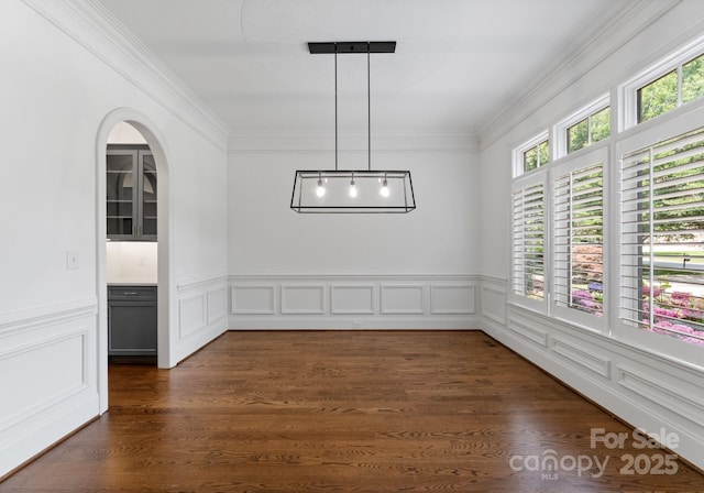1108 Shinnecock Ln, Waxhaw, NC 28173 - unfurnished dining area featuring crown molding, arched walkways, a wainscoted wall, and dark wood-style flooring