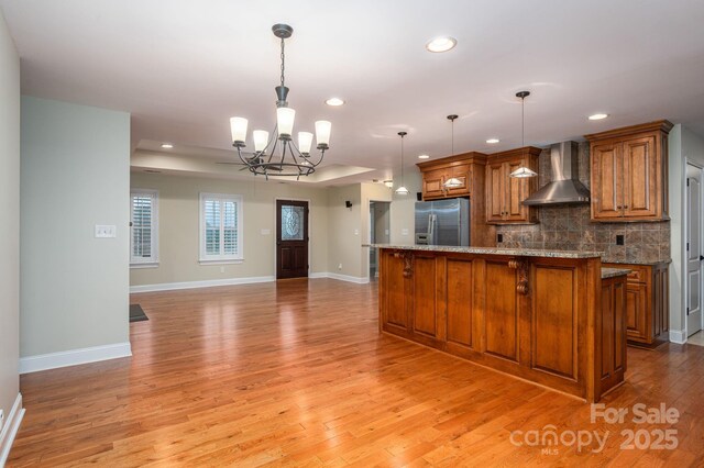 2817 Long Cir Unit 1, Iron Station, NC 28080 - kitchen featuring stainless steel fridge, wall chimney range hood, a chandelier, brown cabinetry, and light wood finished floors