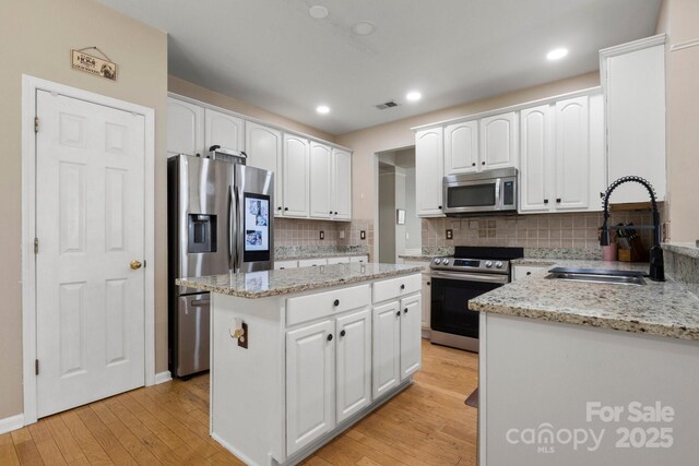 4764 Brockton Ct NW, Concord, NC 28027 - kitchen with stainless steel appliances, a sink, light wood-type flooring, tasteful backsplash, and white cabinets