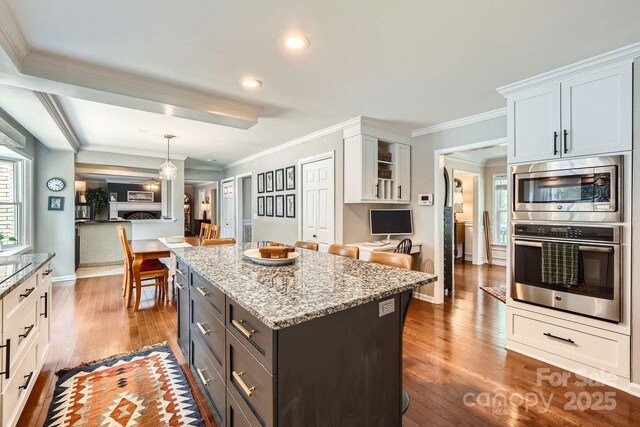 1175 18th Ave NE, Hickory, NC 28601 - kitchen featuring wood-type flooring, stainless steel microwave, a center island, light stone counters, and ornamental molding