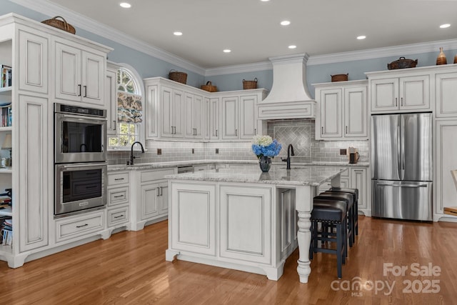 1629 Southpoint Ln, New London, NC 28127 - kitchen featuring stainless steel appliances, premium range hood, light wood finished floors, a center island with sink, and crown molding