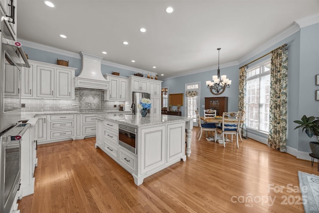 1629 Southpoint Ln, New London, NC 28127 - kitchen with custom exhaust hood, a chandelier, white cabinetry, backsplash, and light wood-style flooring