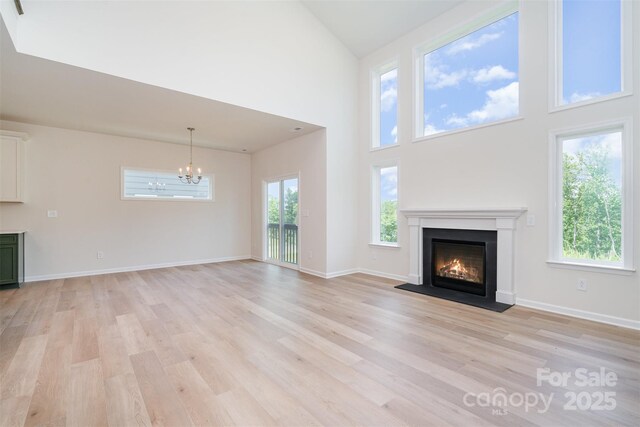 18019 Wilbanks Dr, Charlotte, NC 28278 - unfurnished living room with a chandelier, light wood-type flooring, a warm lit fireplace, a high ceiling, and baseboards