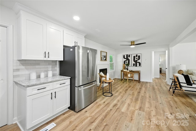 6127 Eagle Peak Dr, Charlotte, NC 28214 - kitchen with freestanding refrigerator, light wood-style floors, a fireplace, white cabinets, and a ceiling fan
