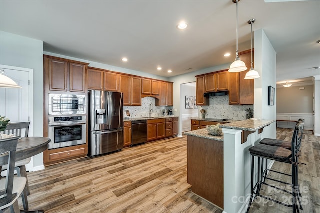 714 Deerbrook Ln, Tega Cay, SC 29708 - kitchen featuring black appliances, a peninsula, brown cabinets, light wood-style floors, and under cabinet range hood