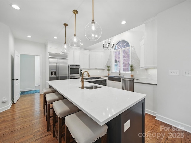 4644 Snow Dr, Harrisburg, NC 28075 - kitchen with stainless steel appliances, a sink, wood finished floors, white cabinets, and a center island with sink