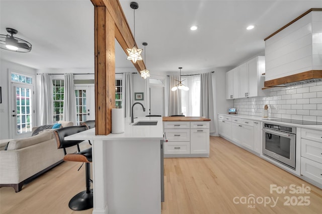 15737 Agincourt Dr, Huntersville, NC 28078 - kitchen featuring oven, a sink, premium range hood, open floor plan, and light wood-type flooring