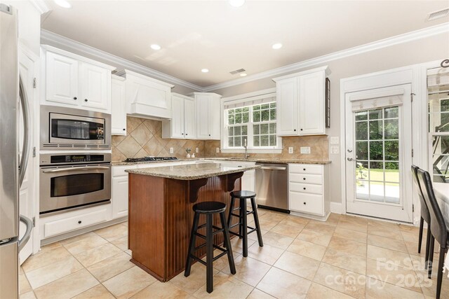 10106 Silverling Dr, Waxhaw, NC 28173 - kitchen with stainless steel appliances, white cabinets, a breakfast bar area, light stone countertops, and ornamental molding